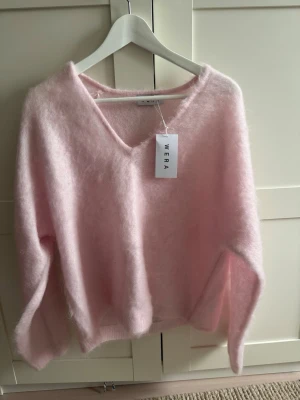 Ljusrosa fluffig stickad tröja Wera - Supermjuk och fluffig stickad tröja från Wera i ljusrosa. Tröjan har v-ringning, lång ärm och avslappnad passform. Perfekt för dig som gillar en cozy och trendig look. Materialet känns lyxigt och ger en riktigt mysig känsla.