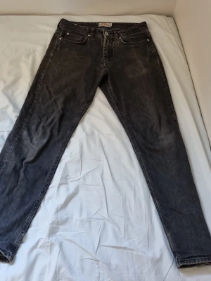 Svarta jeans från Henry Choice - Snygga svarta jeans från Henry Choice med klassisk femficksmodell och raka ben. Jeansen har en tvättad look och silverfärgade detaljer vid knappar och nitar. Perfekta för dig som gillar en avslappnad men stilren stil.