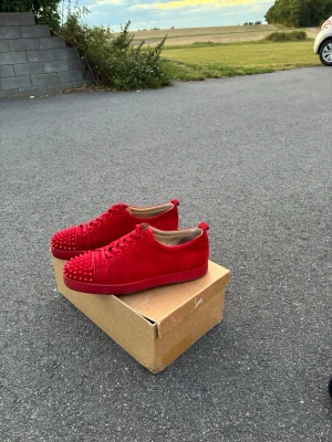 ÄKTA Röda sneakers med nitar Louboutin - Säljer ett par riktigt snygga röda sneakers från Christian Louboutin. Skorna är i mocka med matchande röda nitar på tån och har klassisk låg profil. Kommer med originalkartong, extra skosnören och dustbags. Perfekta för dig som vill sticka ut! Obs BOX ingår tyvärr inte 