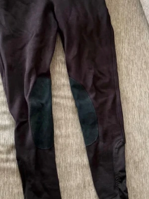 Svarta ridleggings med knäskodd - Säljer ett par svarta ridleggings med förstärkta knäskodda partier i mockaimitation. Tight passform och stretchigt material som ger bra rörelsefrihet. Perfekta för dig som gillar ridning och vill ha bekväma leggings med extra grepp.