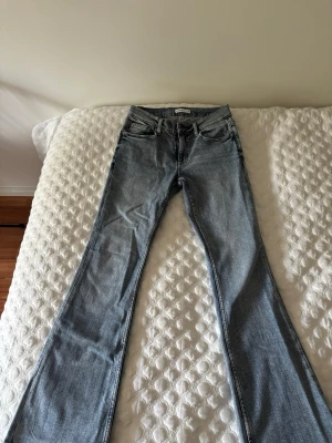 Ljusblå bootcut jeans - Säljer ett par ljusblå bootcut jeans med klassisk femficksdesign och normal midja. Jeansen har en snygg tvättad look och vida ben som ger en retro känsla. Perfekta att styla med sneakers eller boots för en trendig outfit.