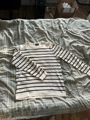 Randig tröja från Massimo Dutti - Snygg långärmad tröja från Massimo Dutti i vit bomull med svarta horisontella ränder. Klassisk rak passform och rund halsringning. Perfekt för en stilren och avslappnad look.