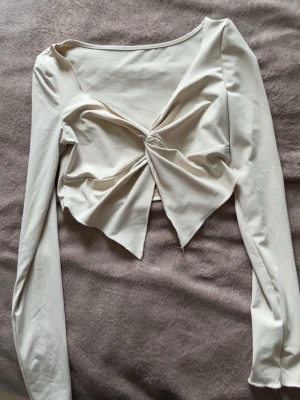 Beige croppad topp med twist framtill - Beige croppad topp med lång ärm och snygg twistdetalj framtill. Toppen har v-ringning och spetsig nederkant som ger en unik look. 