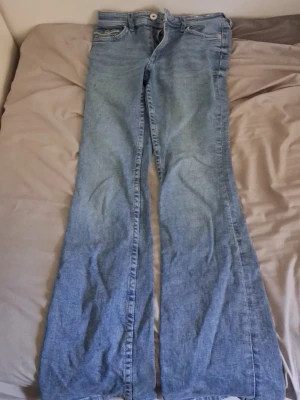 Ljusblå bootcut jeans med fickdetaljer - Säljer ett par ljusblå bootcut jeans med klassisk femficksdesign och snygga detaljer på bakfickorna. Jeansen har mellan midja och vida ben, perfekta för en avslappnad och trendig look. Tillverkade i denim med knapp- och dragkedjestängning. Har dock små fläckar på framsidan!