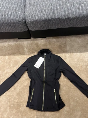 Lululemon svart zip-up jacka med gulddetaljer – storlek 6/L - Storlek 6 / L  Längd 53 cm  Bröstvidd 84 cm  Nederkant 74 cm    Lululemon zipup i mycket bra skick 
