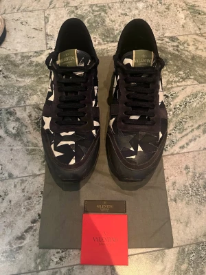 Valentino Rockrunners - Snygga sneakers från Valentino med mörkblå bas och vita stjärnmönster. Skorna har svarta snören, vita detaljer på hälen med nitar i form av en stjärna och en robust sula. Materialmix av textil och läder ger en exklusiv känsla och unik look. Skorna har en liten defekt i hälen av skon där det skavts upp av användning. Förutom det är de i väldigt fint skick. 