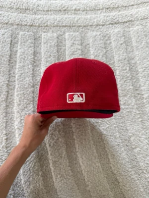 Röd fitted-keps med MLB-logga - Snygg röd basebollkeps med klassisk rak skärm och broderad MLB-logga baktill. Kepsen har ventilationshål och är tillverkad i ett tåligt tygmaterial. Perfekt för dig som vill ha en stilren och sportig look.
