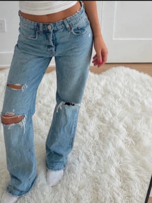 Blå ripped jeans från g perfect jeans - Säljer ett par ljusblå jeans från g perfect jeans i storlek 34. De har raka ben och slitna detaljer med hål på båda benen. Klassisk femficksmodell och tillverkade i denim. Perfekta för en avslappnad och trendig look.