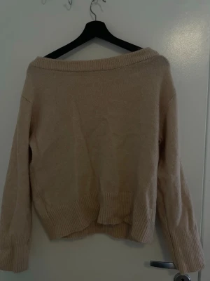 Beige off shoulder stickad tröja - Stickad tröja från Gina Tricot i en mjuk beige färg. Tröjan har off shoulder-modell, långa ärmar och bred ribbstickad kant vid ärmslut och nederkant. Perfekt för en avslappnad och trendig look.