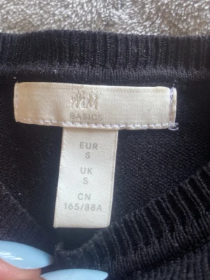 Stickad T-shirt - En enkel svart stickad tröja från H&M Basics i storlek S. Tröjan har rund halsringning och korta ärmar. Materialet är mjukt och passar perfekt till lager på lager. Klassisk och stilren design som funkar till det mesta.