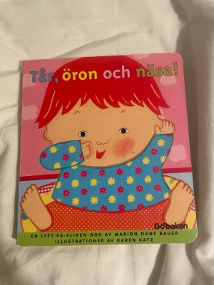 Tår, öron och näsa! pekbok - Färgglad pekbok för små barn med titeln 'Tår, öron och näsa!'. Boken har tjocka kartongsidor och illustrationer av Karen Katz. Den innehåller lyft-på-fliken-funktioner och är utgiven av Goboken. Perfekt för att lära sig om kroppen på ett lekfullt sätt.