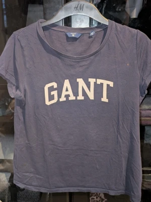 Blå GANT t-shirt med tryck - Säljer en mörkblå t-shirt från GANT med klassiskt vitt tryck framtill. T-shirten har rund halsringning och korta ärmar. Tillverkad i mjuk bomull för en skön känsla. En liten fläck vid bröstet som säkert gå bort i tvätten 