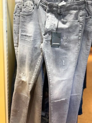 Grå slitna jeans från Dsquared2 - Snygga grå jeans från Dsquared2 med slitna detaljer och diskreta tryck framtill. Jeansen har klassisk femficksmodell, raka ben och normal midja. Materialet är mjukt denim som ger en avslappnad look. Perfekta för dig som gillar streetstyle.