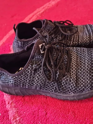 Svarta stickade sneakers med snörning - Säljer ett par svarta sneakers med stickad ovandel och vita detaljer i mönstret. Skorna har svarta snören och en svart sula. Lätta och flexibla, perfekta för en avslappnad stil. Passar dig som gillar sportig look och komfort.