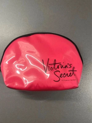 Rosa necessär från Victoria's Secret - Snygg rosa necessär från Victoria's Secret i glansigt material med svart dragkedja och logga framtill. Perfekt för smink eller småprylar.  Finns en genomskinlig fläck inuti som jag tror är från nagellack.