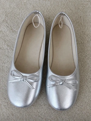 Silvriga ballerinaskor med rosett - Snygga ballerinaskor i silver med rund tå och rosett. Använda två gånger inomhus och är i nyskick! Storlek 37