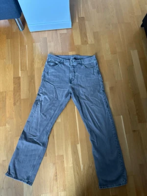 Grå raka jeans med fem fickor - Säljer ett par grå jeans med klassisk femficksmodell och raka ben. Jeansen har normal midja och stängs med dragkedja och knapp. Materialet är denim i bomull och de har en avslappnad passform som funkar till många stilar. Fickorna är smått insydda