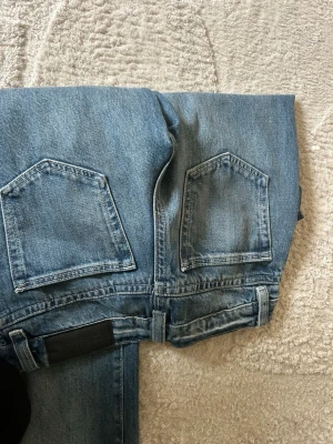 Blå raka jeans  - Säljer ett par klassiska blå jeans  med raka ben och femficksmodell. Jeansen har tydliga sömmar, bälteshällor och en snygg tvättad look. Perfekta för en avslappnad och stilren outfit.