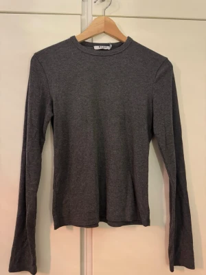 Grå ribbad tröja från NA-KD - Säljer en enkel och stilren grå långärmad tröja från NA-KD. Tröjan är ribbad och har en rund halsringning. Perfekt att matcha med jeans eller kjol för en clean look.