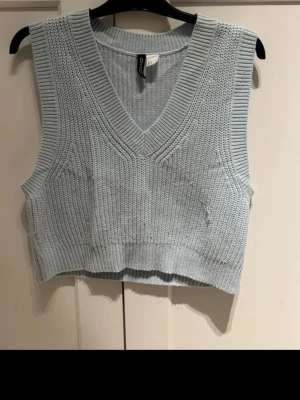 Ljusblå stickad väst från Divided - Snygg ljusblå stickad väst från Divided med v-ringad hals och ribbade kanter. Perfekt att bära över en skjorta eller t-shirt för en trendig lager-på-lager-look. Croppad modell som ger en modern vibe.