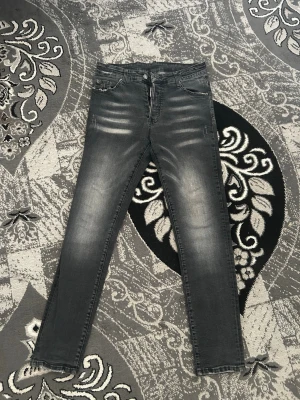 Dsquared2  - Säljer ett par grå slim fit jeans med snygga slitningar och tvättade detaljer. Jeansen har fem fickor, bälteshällor och dragkedjegylf. Perfekta för en avslappnad och trendig look.