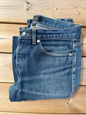Blå raka jeans från A.P.C. - Snygga blå jeans från A.P.C. i klassisk rak modell. Jeansen har fem fickor, silverfärgade nitar och knapp, samt tydliga kontrastsömmar. Tillverkade i slitstark denim med en tvättad finish som ger en cool vintagekänsla. Mycket bra skick men har fortfarande används. Kan tänka mig att sänka pris