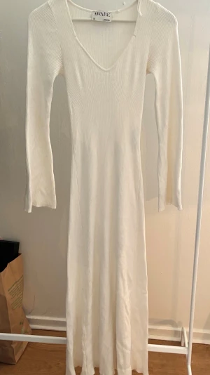 Vit ribbad långklänning  - Lång, vit ribbad klänning med v-ringning och långa ärmar. Klänningen har en smickrande passform och är tillverkad i ett mjukt, stretchigt material som ger en bekväm känsla. Perfekt för dig som gillar stilrena och enkla plagg.