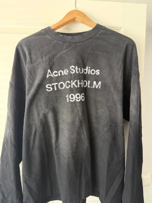 Acne Studio Svart långärmad M - Cool svart långärmad t-shirt från Acne Studios med tryck 'Acne Studios STOCKHOLM 1996' på bröstet. Oversized fit och rund halsringning. Perfekt för dig som gillar streetwear och vill ha en stilren men ändå statement look.