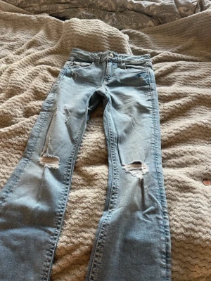 Ljusblå jeans - Säljer min lillasysters gamla ljusblåa jeans med raka ben och hål på båda knäna. Jeansen har klassiska fem fickor och bakfickor med lock och knapp. Perfekta för en avslappnad och trendig look. Storlek 158 från Gina Tricot. Mid - high waisted och aldrig nånsin använda. 