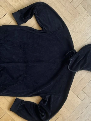 Svart hoodie i mjuk velour - Säljer en svart hoodie i mjuk velour med huva och dragsko ifran You Turn. Hoodien har en stor magficka och ribbade muddar vid ärmslut och nederkant. Perfekt för en chill och avslappnad stil.