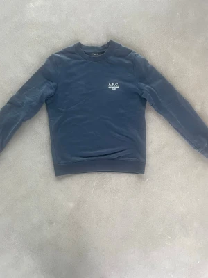 Mörkblå sweatshirt från A.P.C. - Snygg mörkblå sweatshirt från A.P.C. med rund halsringning och diskret logga på bröstet. Tillverkad i mjukt material och har klassisk passform med långa ärmar och ribbade muddar. Perfekt för en clean och stilren look. Köpt på NK