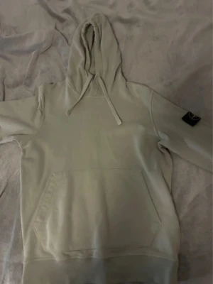 Stone Island Hoodie  - Snygg beige hoodie med stor magficka och justerbar luva. Klassisk design med ribbade muddar och patch på ena ärmen. Perfekt för chill dagar eller när du vill ha en clean look.