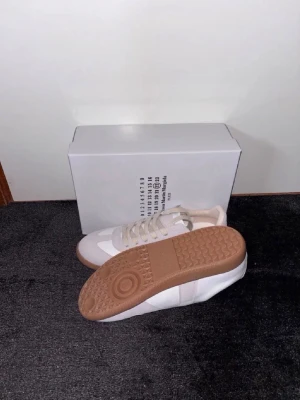 Vita och beige sneakers med gummisula - Snygga sneakers i vitt och beige med klassisk design och beige gummisula. Ovandelen är i en mix av mocka och slätt material, med matchande beige snören. Perfekta för dig som gillar stilrena och tidlösa skor.