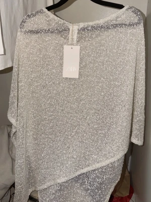 Vit glittrig poncho från Zara ny med prislapp  - Säljer en superfin vit poncho från Zara med glittereffekt. Ponchon är tunn, transparent och har en lös, avslappnad passform med breda ärmöppningar. Perfekt att styla över ett linne eller topp för en trendig look. Helt ny med prislapp 