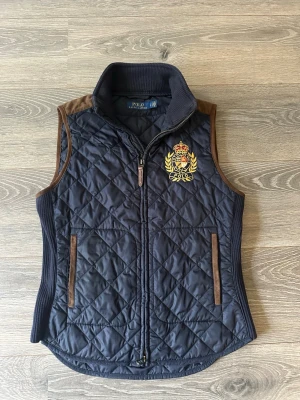 Marinblå väst Polo Ralph Lauren - Marinblå väst från Polo Ralph Lauren med brunt mocka vid axlar och fickor. Bra skick, Strl S