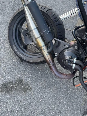 Trimrör aerox - Säljer ett avgassystem till moped med svart ljuddämpare och böjt rör i metall. Passar till bakhjulet på de flesta mopeder och har en sportig look. Monteringsdetaljer och fjädring syns på bilden. Perfekt för dig som vill uppgradera din moppe.