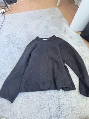 Svart stickad tröja från Gina Tricot - Mysig svart stickad tröja från Gina Tricot i ullblandning. Tröjan har rund halsringning, långa ärmar och ribbade muddar vid ärmslut och nederkant. Perfekt för kyliga dagar och enkel att matcha med olika outfits.