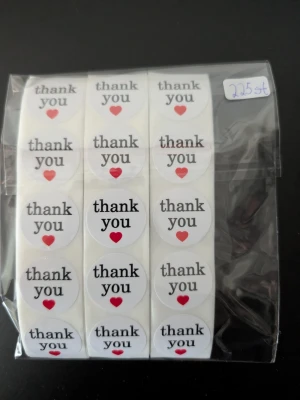 Runda thank you-klistermärken 225 st  - Säljer ett paket med runda vita klistermärken med texten 'thank you' och ett rött hjärta under. Perfekta för paket, brev eller presenter. Kommer i en genomskinlig plastförpackning och innehåller flera ark med etiketter.