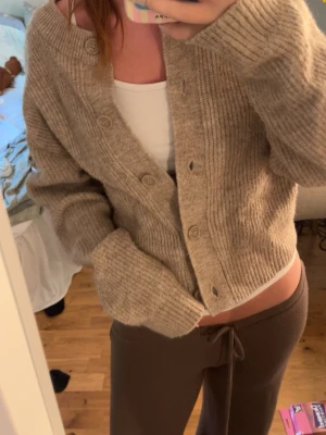 Beige ribbstickad kofta med knappar - Mysig beige kofta i ribbstickat material med rund halsringning och knäppning framtill. Koftan har en avslappnad passform och långa ärmar, perfekt att slänga över ett linne eller t-shirt. Passar till både jeans och mjukisbyxor.