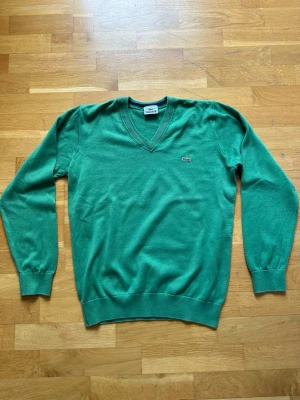 Grön Lacoste Tröja - En mycket fin grön v-ringad tröja från Lacoste.  Storlek: 3/Small Passform: Normal Skick: Väldigt fint skick, inga hål eller fläckar.  Har du några frågor eller vill ha fler bilder? Tveka inte på att höra av dig!