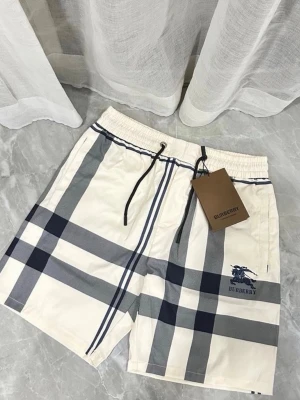 Rutiga shorts från Burberry - Snygga shorts från Burberry i klassiskt rutigt mönster med beige, grå och mörkblå toner. Shortsen har snörning i midjan och är perfekta för en trendig och avslappnad stil. Ikoniska Burberry-loggan på benet ger en exklusiv touch.