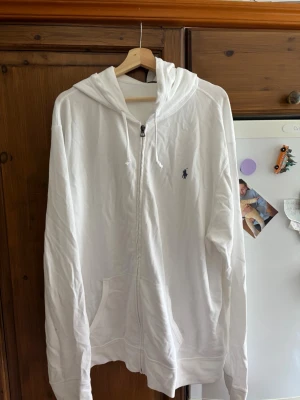 Vit hoodie från Polo Ralph Lauren - Säljer en vit hoodie från Polo Ralph Lauren i storlek XXL. Hoodien har dragkedja framtill, två fickor och den klassiska Polo-loggan broderad på bröstet. Tillverkad i mjukt material och har huva med dragsko. Perfekt för en avslappnad och stilren look.