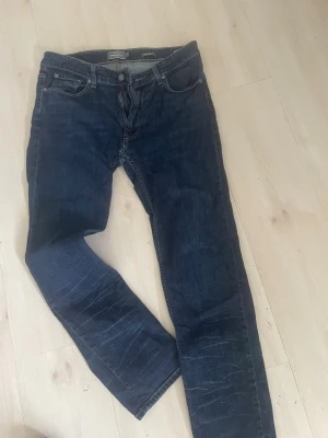Mörkblå jeans från Dressmann - Snygga mörkblå jeans från Dressmann i regular fit. Klassisk femficksmodell med dragkedjegylf och kontrastsömmar. Jeansen är tillverkade i slitstarkt denimtyg och har diskreta slitningar för en cool look.