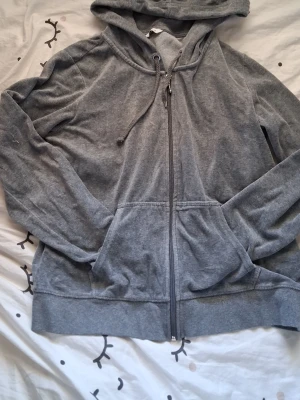 Grå zip hoodie med huva - En enkel och stilren grå hoodie med dragkedja framtill och två stora fickor. Hoodien har en justerbar huva med snören och ribbade muddar vid ärmslut och nederkant. Perfekt för en avslappnad look och passar till det mesta.