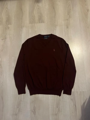 Vinröd merinoullströja Polo Ralph Lauren - Vinröd stickad tröja från Polo Ralph Lauren i slim fit-modell, tillverkad av tvättbar merinoull. Tröjan har långa ärmar och den klassiska lilla logotypen broderad på bröstet. Perfekt för en stilren och bekväm look.