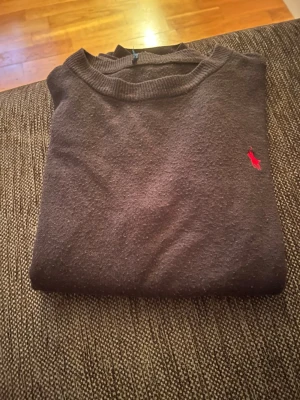 Svart stickad polo Ralph Lauren tröja - Klassisk svart stickad tröja med rund hals och den klassiska loggan🤩 Tröjan har långa ärmar och ribbade muddar vid ärmslut och nederkant. Perfekt till höst och vinter för en stilren look😅
