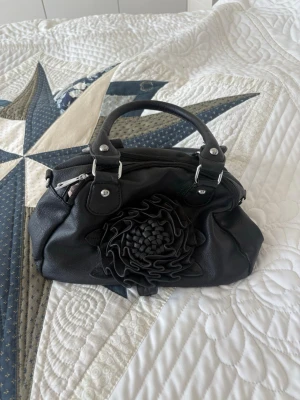 Svart handväska med blomdetalj - Så fin handväska!!🫶🏻 Min mammas gamla så det finns tydliga tecken på användning men inga defekter🩷 buda gärna😊