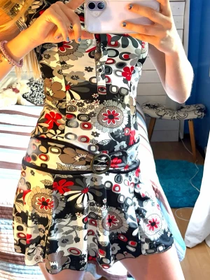 Blommig kortklänning med bälte - Säljer en unik klänning med coolt bälte och volandkjol samr små knappar med fin krage upptill. Skönt material och stretchigt som andas lätt perfekt till sommar!😍 i klänningen står det storlek S/M🤍