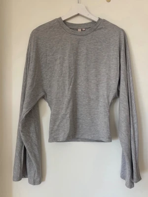 Topp med vida ärmar och markerad midja  - Säljer en ljusgrå croppad topp med rund hals och supervida långärmar. Toppen har en clean look och är gjord i mjukt bomullsliknande material. Perfekt för dig som gillar en chill och trendig stil.