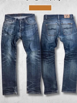 Nudie Jeans, W29 L30 Grim Tim dry deep selvedge - Säljer ett par klassiska blå jeans från Nudie Jeans med snygga slitningar och kontrastsömmar. Jeansen har rak passform, fem fickor och läderpatch bak i midjan. Tillverkade i slitstarkt denim, perfekta för en avslappnad stil.